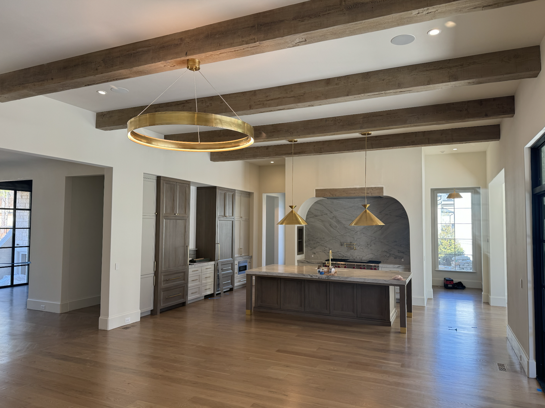 Modern kitchen with wooden ceiling beams, a marble backsplash, an island with a dark wood base, and gold pendant lighting.