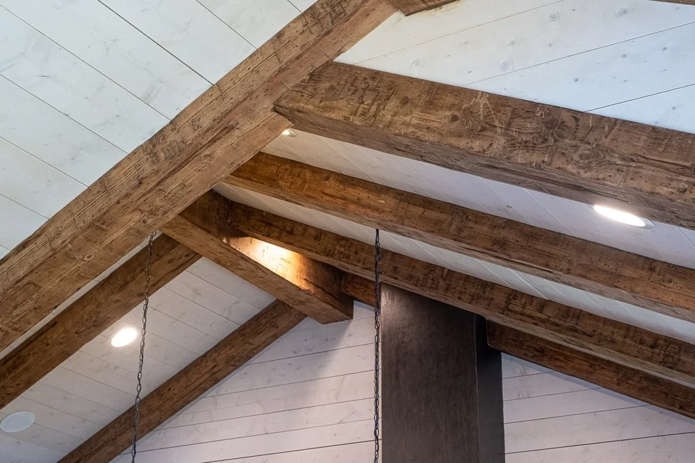 Ceiling with exposed wooden beams and white shiplap paneling, with recessed lighting fixtures.
