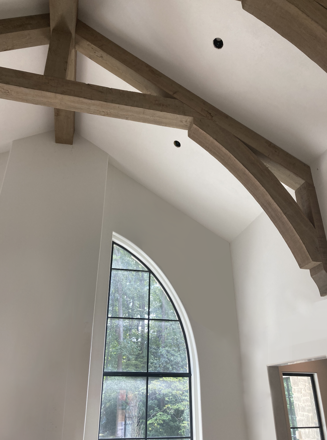 Interior view of a room with a curved wood beam ceiling, a large arched window, and white walls.