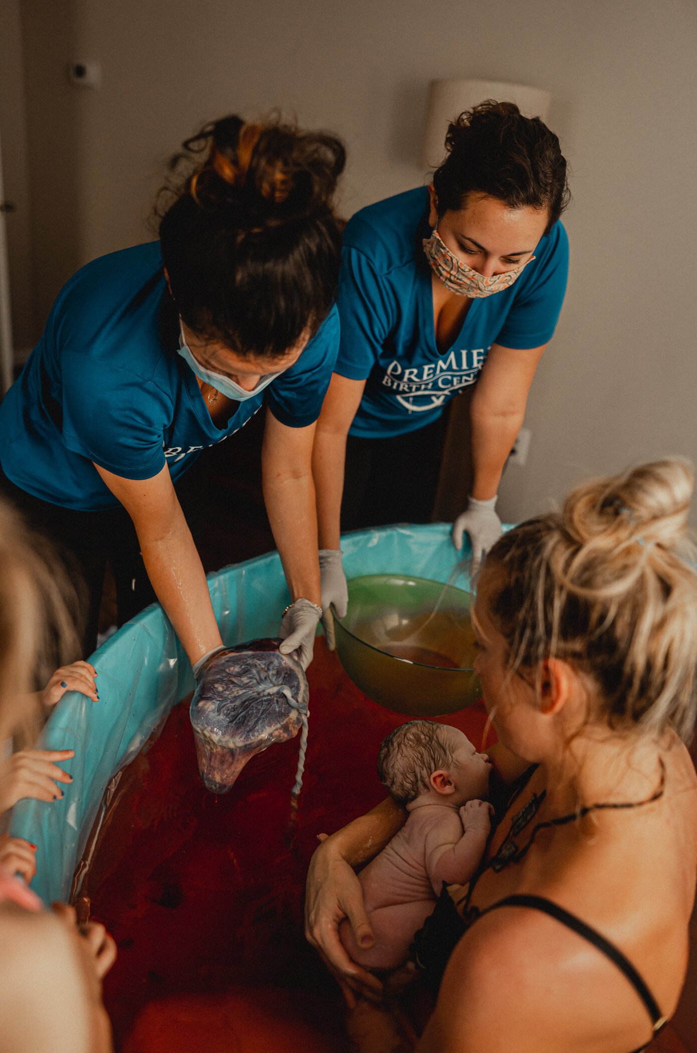 After the placenta is delivered the midwife of premier Birth Center shows off the placenta to the mom who is sitting in the birth pool and her older children who are standing besides her