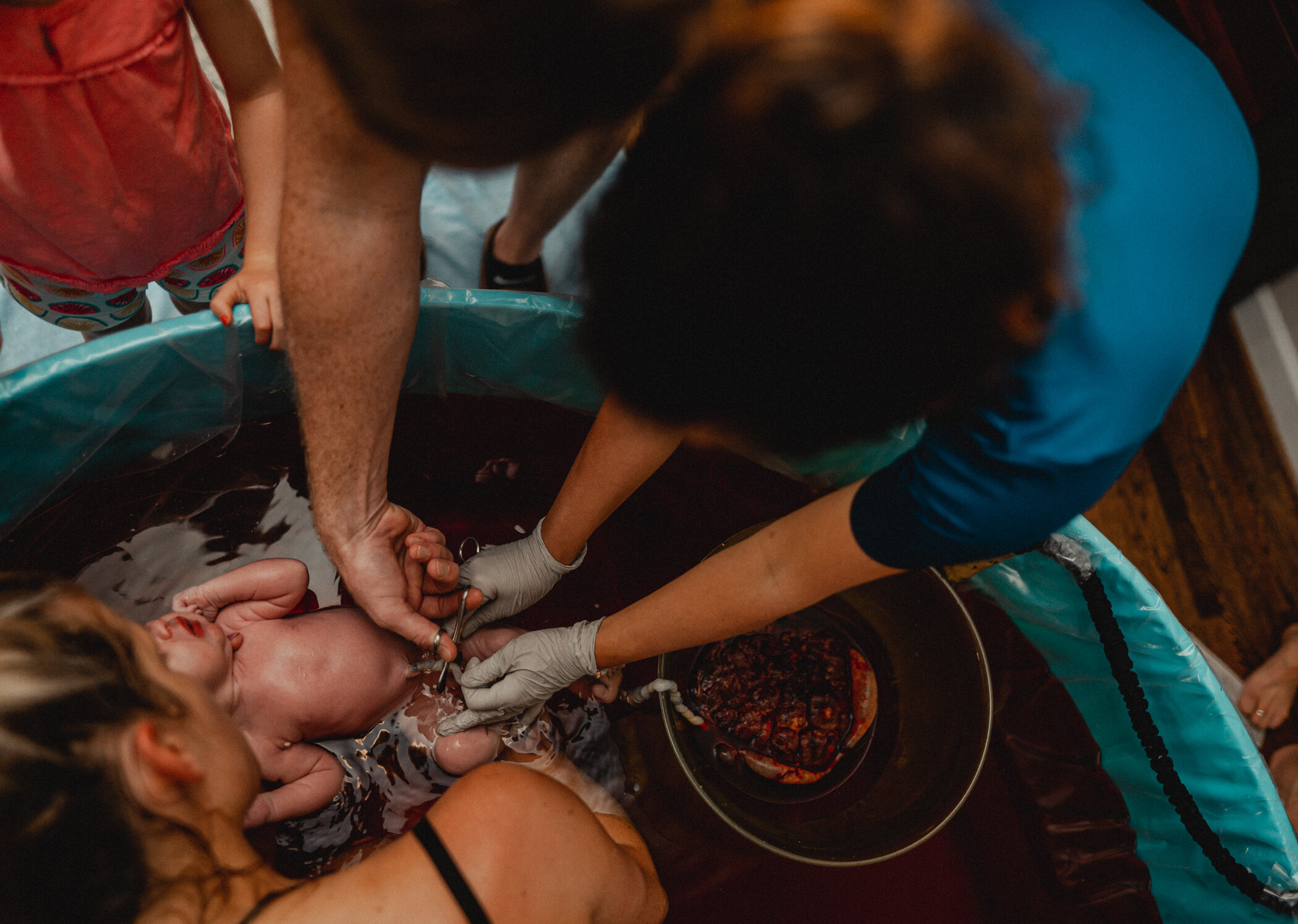 Dad is cutting the umbilical cord after a home water birth in Great Falls, VA with Premier Birth Center. Baby is still floating in the birth tub with his placenta in a bowl next to him