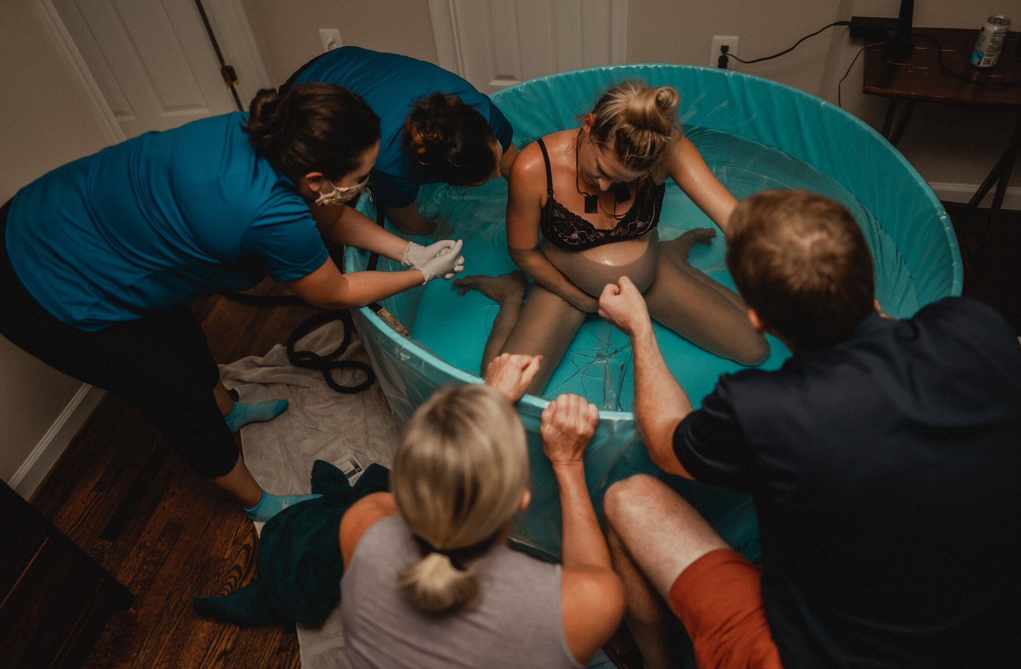 Woman sitting in the birth tub with a transition contraction beginning. Her birth team consisting of her midwife assistant, midwife, mother and husband kneeling along the birth pool to cheer her on 
