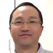 A person with glasses smiling in a well-lit indoor setting.