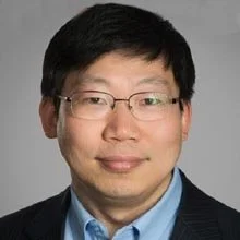 Portrait of a person wearing glasses and a suit jacket against a gray background.