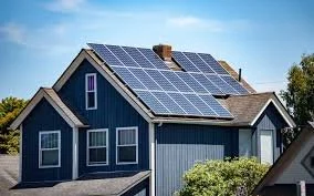 A blue house with solar panels on the roof and a chimney, under a clear sky.