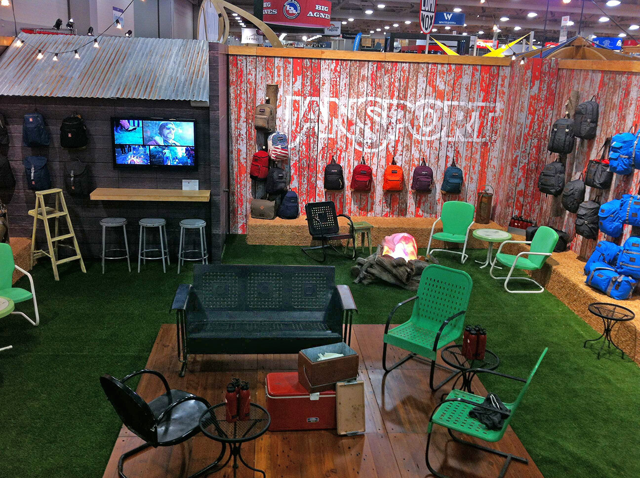 Final booth interior: center stage for music/live bands and sales meetings, storage "shack" with video display featuring campaign sequences, perimeter lined with hay stacks for display and seating, decor of vintage patio furniture, coolers, patio lig