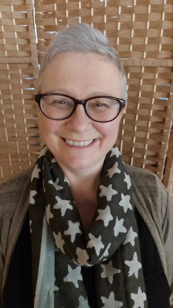 White woman with black glasses wearing a gray scarf with white stars.
