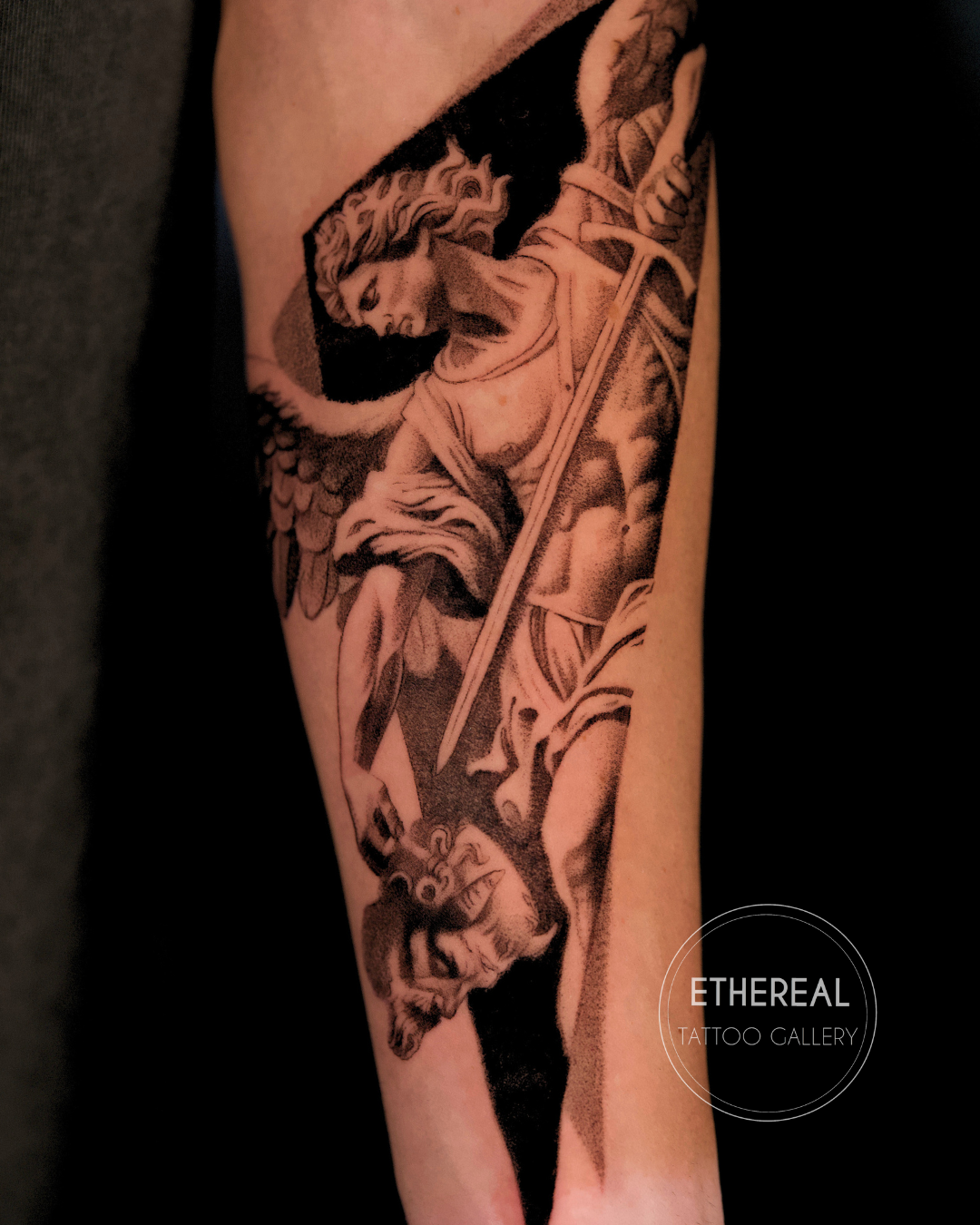 Fine line black and grey Archangel Saint Michael tattoo in realistic microrealism style, depicting Saint Michael defeating a demon, tattooed on the forearm by Brian Parrillo at Ethereal Tattoo Gallery in Durham, North Carolina.