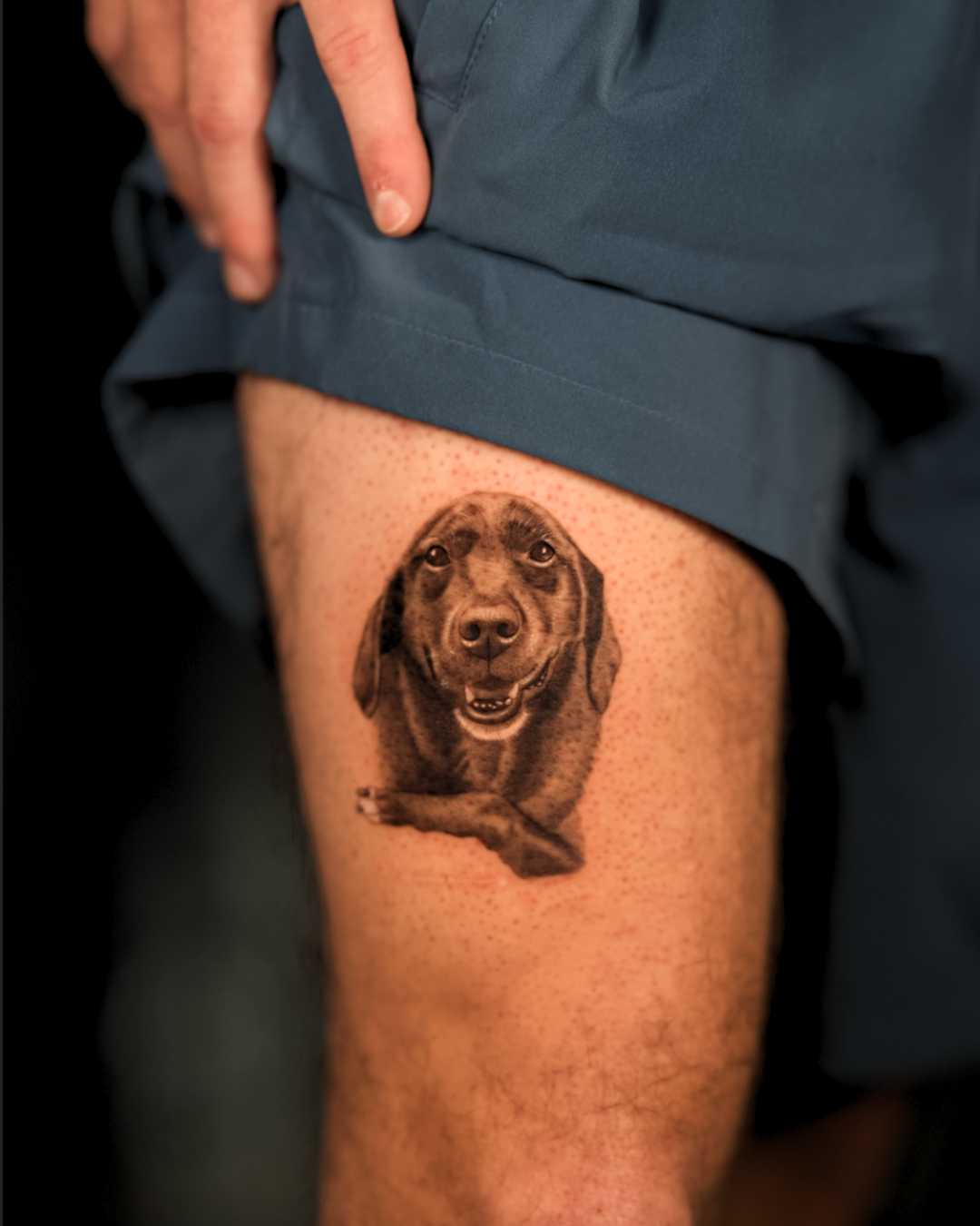 The client wanted to include the dog's paw to show her body position. Small realistic dog portrait tattoo in black and grey on the thigh.