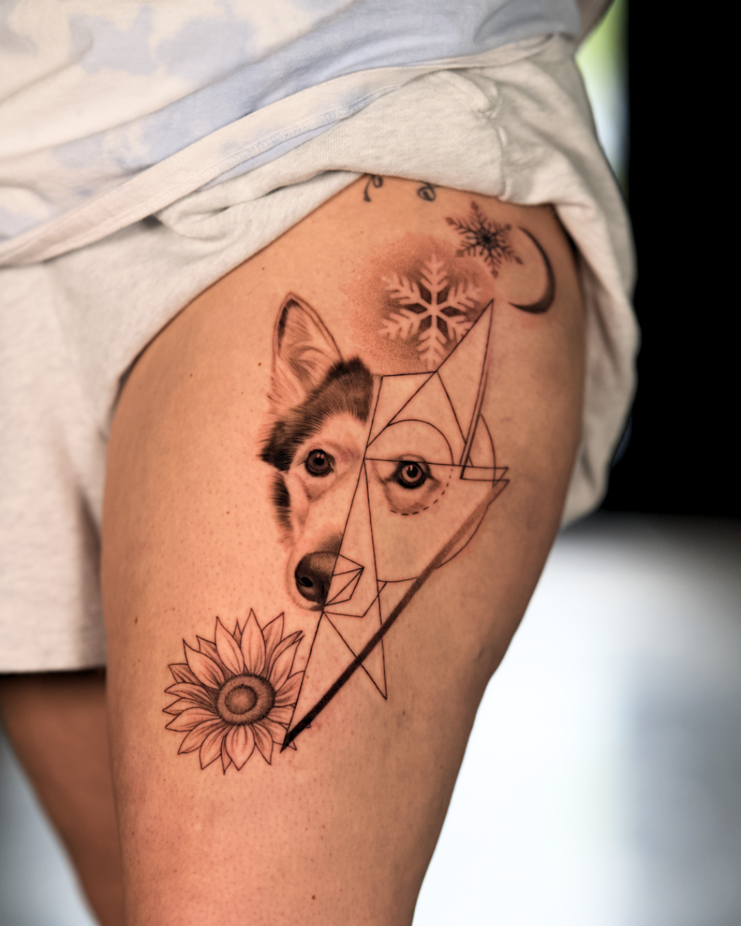Black and grey husky pet portrait tattoo with geometric linework and floral details on thigh.