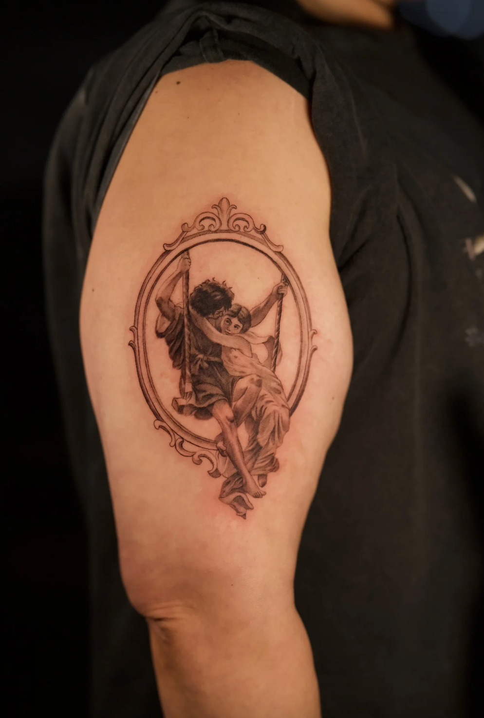 Fine line microrealism tattoo inspired by classical art, showing a romantic couple on a swing framed in an oval, tattooed by Brian Parrillo at Ethereal Tattoo Gallery in Durham, North Carolina.