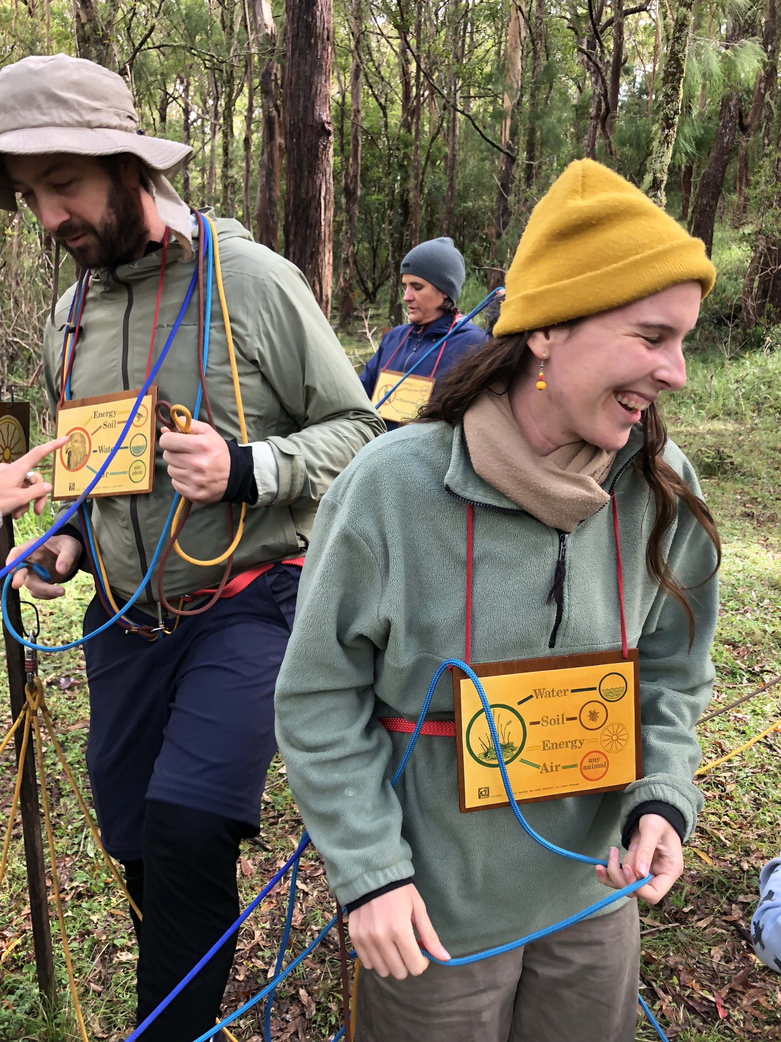 People smiling in nature playing a game with connective ropes and wooden boards hanging around their necks with string.