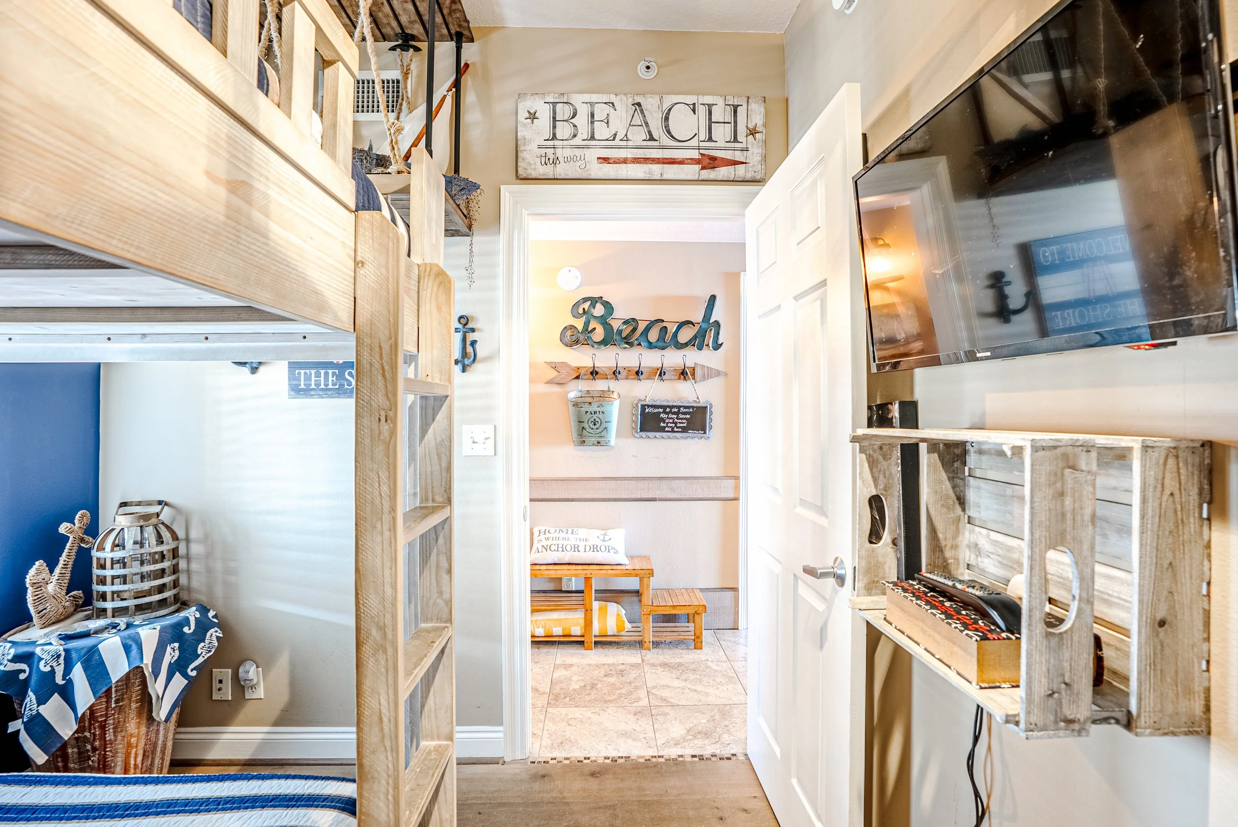 Beach-themed decor in a room with wooden shelves, signs reading 'BEACH this way' and 'Beach', a small wooden bench with cushions, and nautical accessories including a lantern and coral decorations.