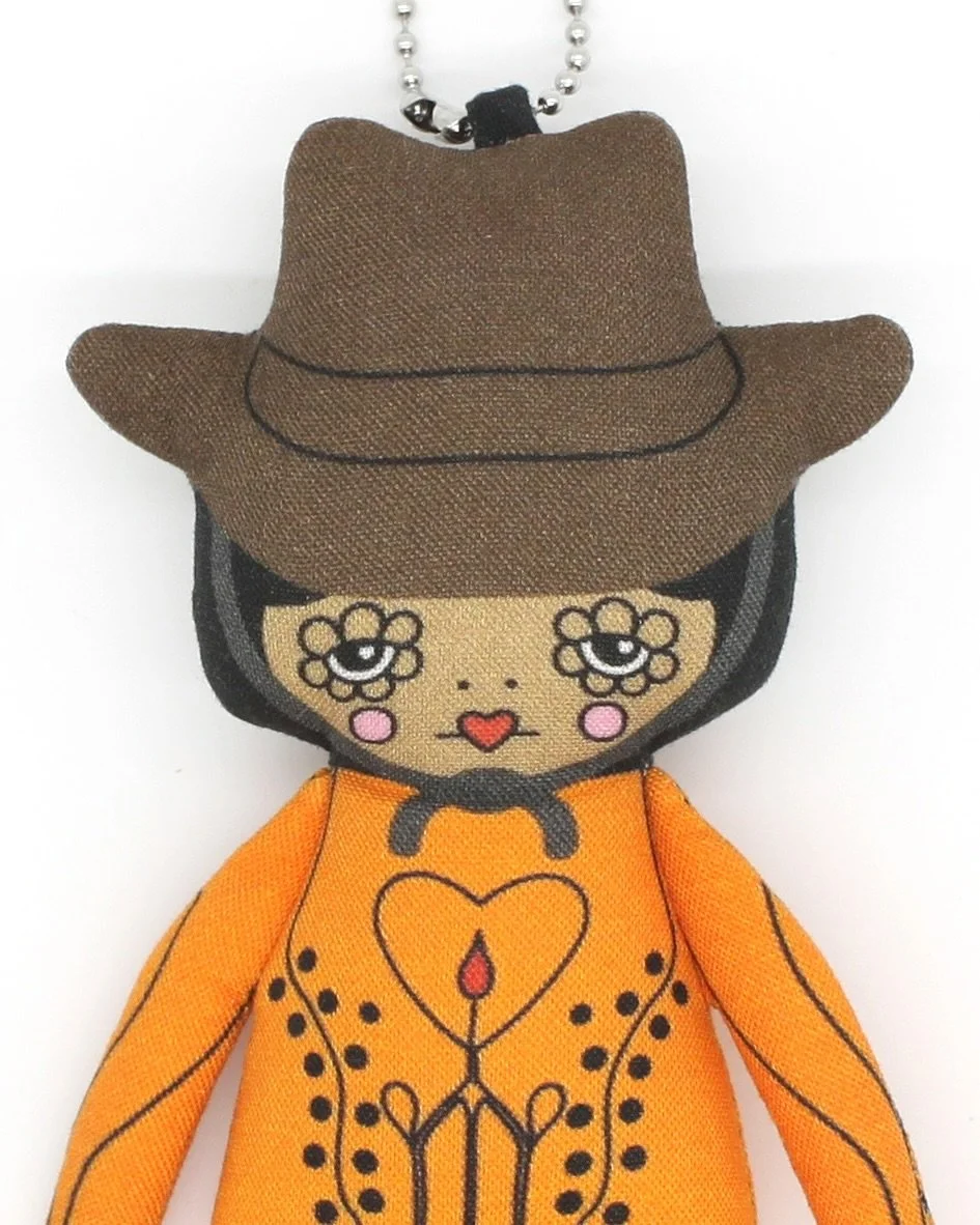 The Cowgirl Dolls are finally a-comin’!
She’s wearing the cutest orange jumpsuit with my drawing of a nudie-inspired cow skull, featuring a little drop of blood and a big bow. The look is complete with a 10-gallon hat and black knee boot