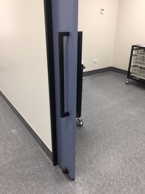 Partially open door with black handle in an empty room with gray carpet, white walls, and a black rolling cart.