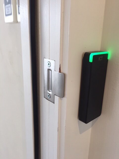 Card access control device next to door frame with green light indicator.