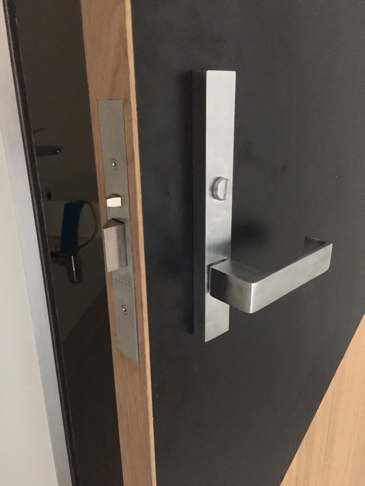 Close-up of a black door with a modern stainless steel door handle and lock, viewed from the side.
