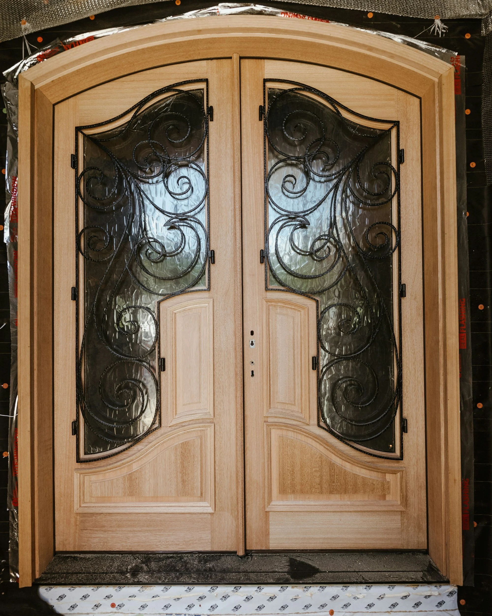 A double wooden front door with glass panels and decorative black wrought iron scrollwork.