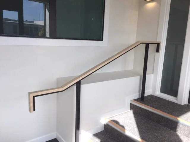 Exterior view of a modern building with a ramp for accessibility, featuring a black handrail and a window.