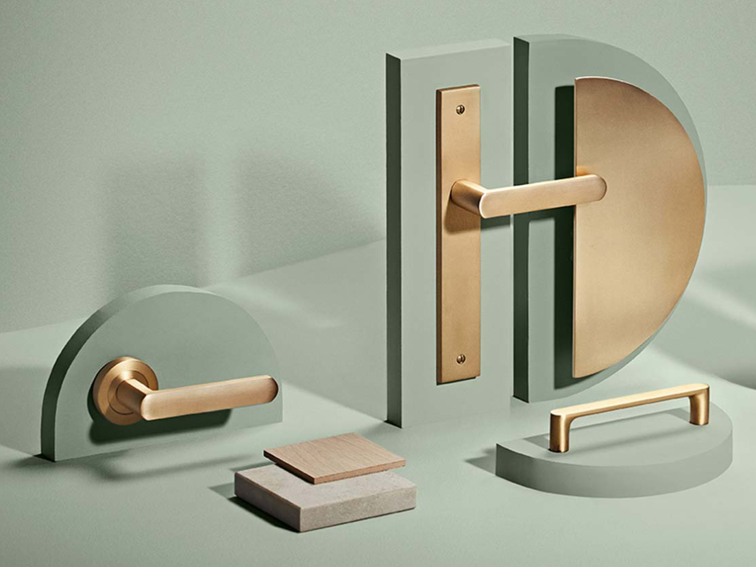 Minimalist modern door handle set with gold accents, mounted on green geometric blocks with tiles in front, against a light green background.