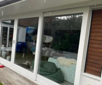 Sliding glass doors leading to a deck, with a view into a room containing a sofa and various objects inside a house.