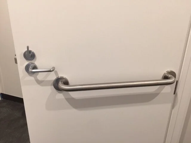 A white door with a silver handle, lock, and a horizontal grab bar attached.