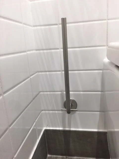 Toilet paper dispenser and grab bar in a public restroom with white tiled walls.