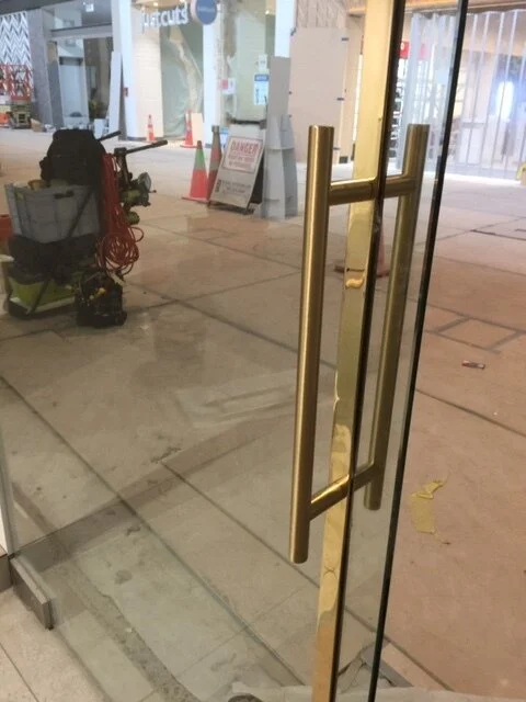 Glass door with brass handle in a storefront, with construction equipment and orange cones visible outside.
