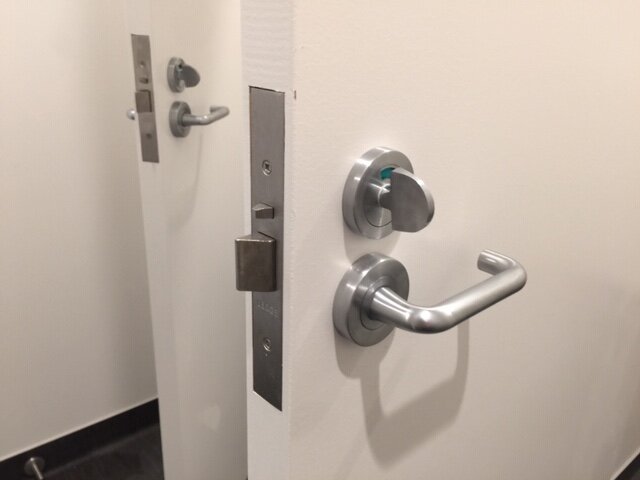 A door with a lock, deadbolt, and security handle, seen from an internal side at an office building.