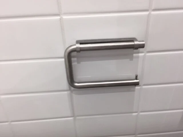 Empty metal toilet paper holder on white tiled wall.