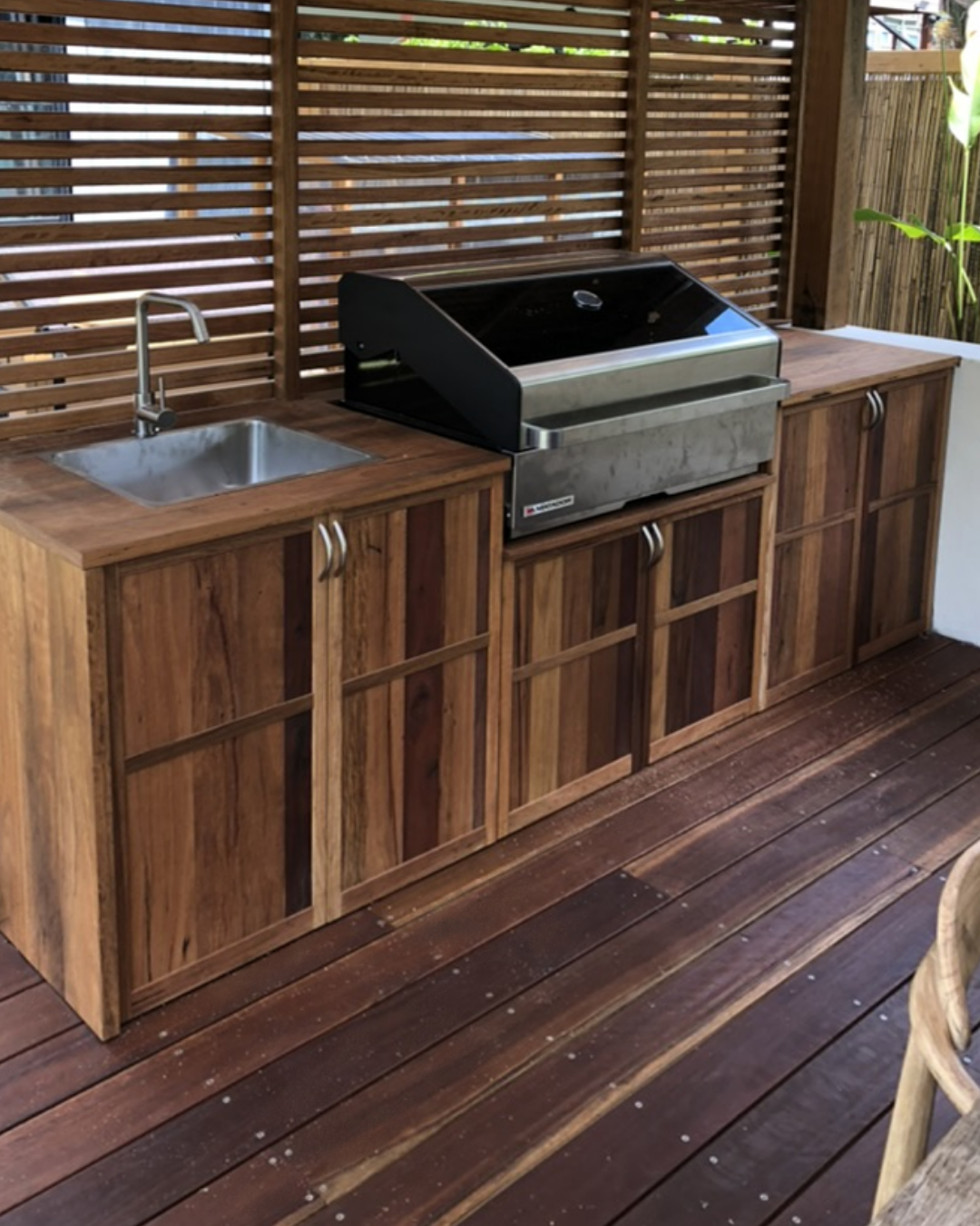 Outdoor kitchen with wooden cabinets, a small sink, a grill, and a wooden slat privacy fence.