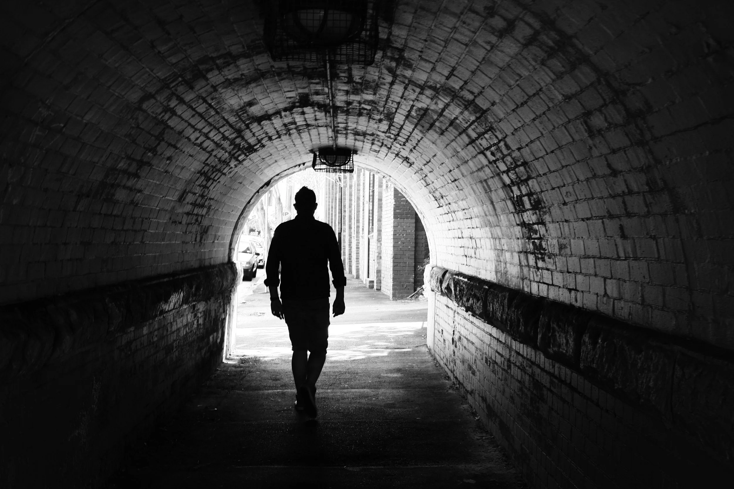 A silhouette of a person walking through a brick tunnel towards a brighter outdoor area.