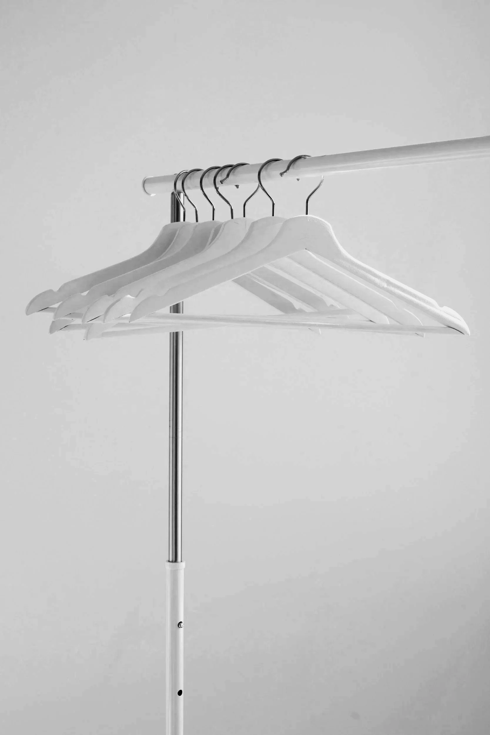 Several white clothes hangers on a metal clothing rack against a plain background.