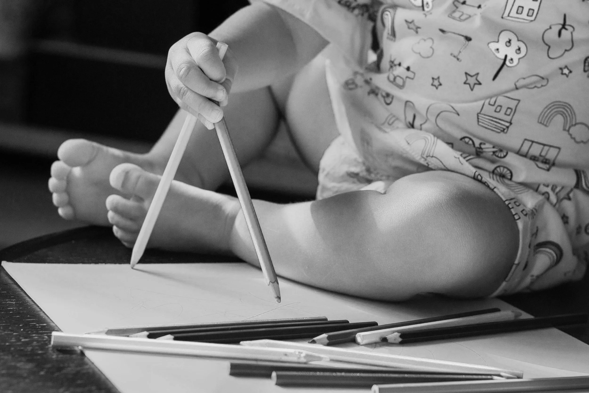 Child playing with coloured pencils on a table, with paper and pencils scattered around.