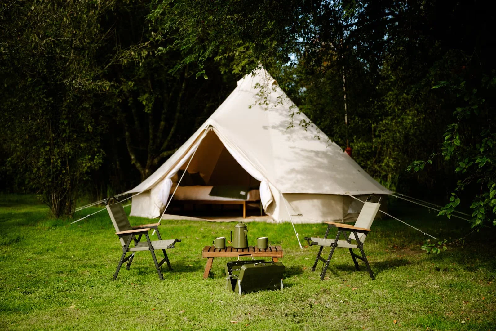 A private yurt with two chairs and a table with two cups and a pitcher situated in the forest.