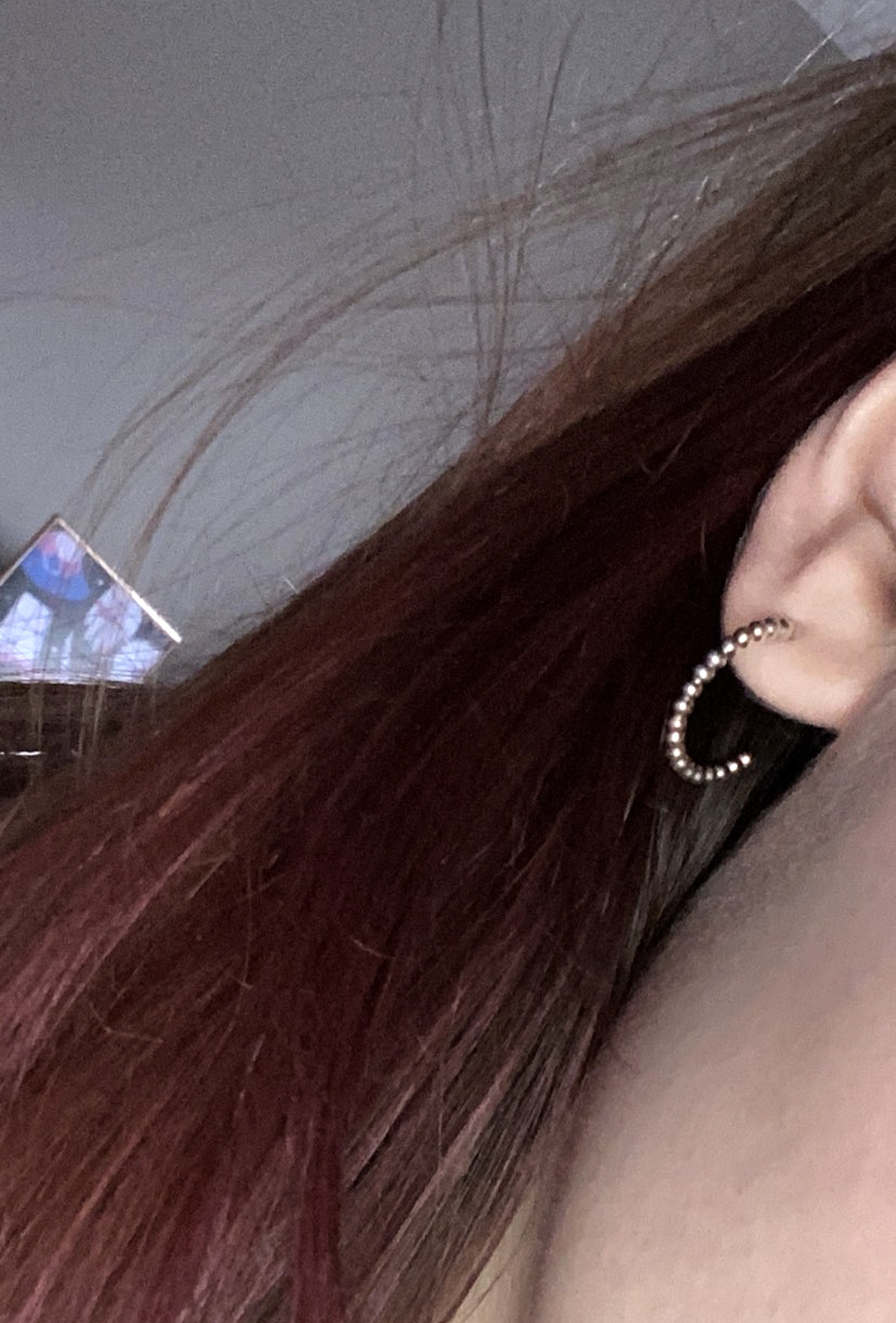 Close-up of a person's ear with a pearl hoop earring, reddish-brown hair, and a TV screen in the background.