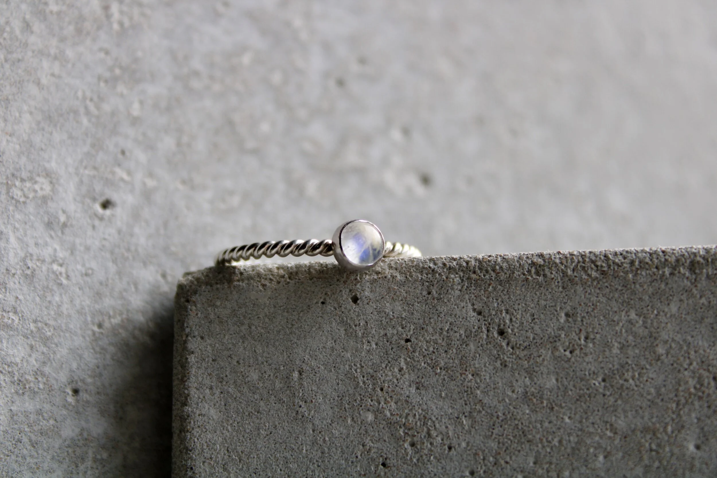 Silver ring with a round, translucent gemstone resting on a concrete surface.
