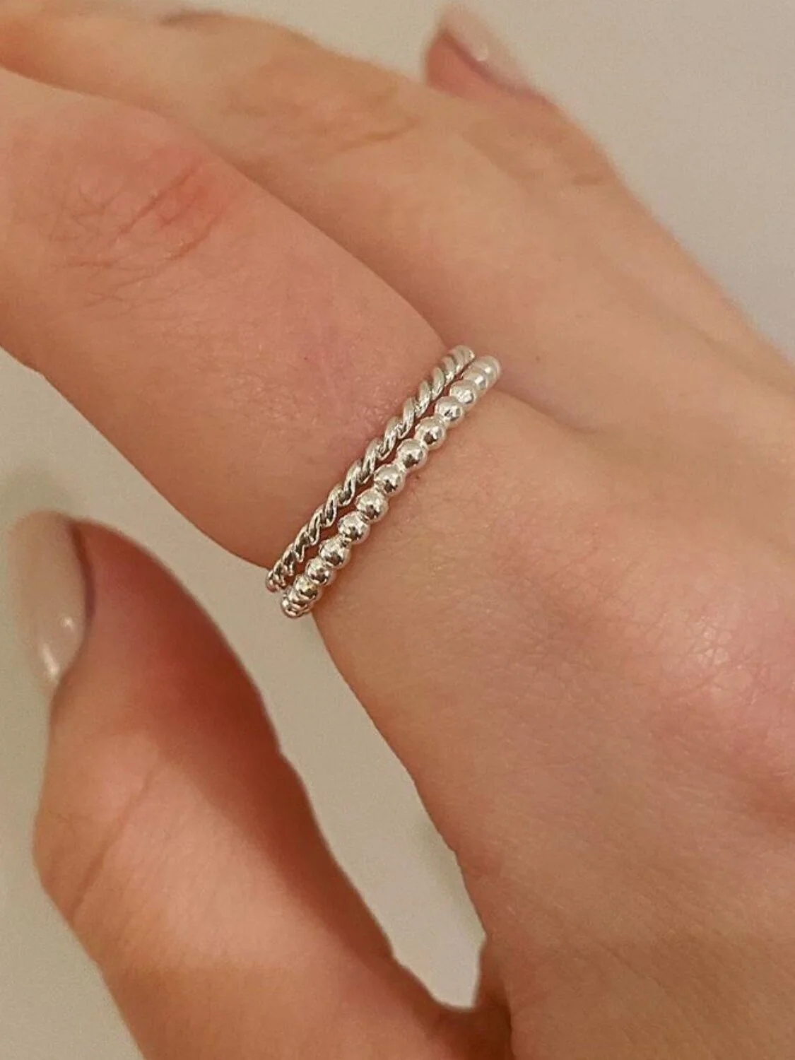 Two silver rings on a person's middle finger, one with a twisted design and the other with a smooth, rounded surface.