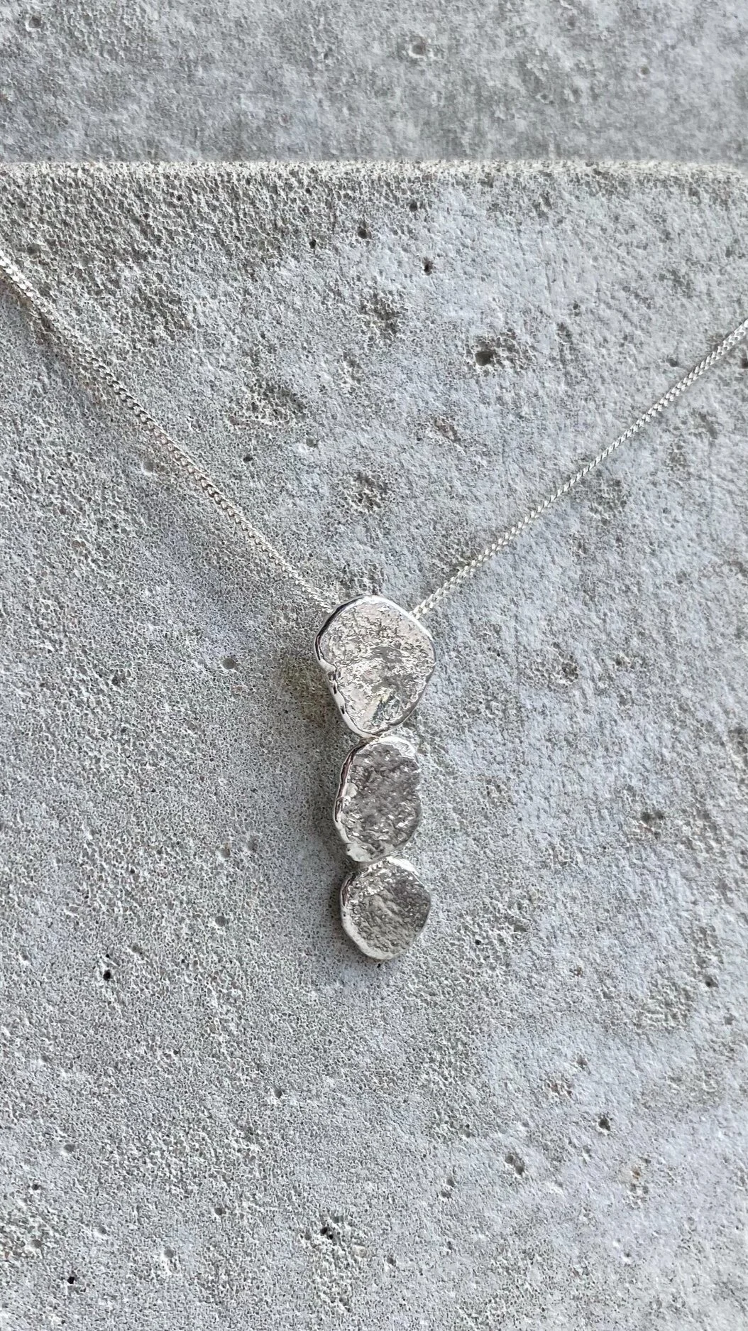 Silver necklace with three rough-cut, irregularly shaped clear stones displayed on a textured grey background.