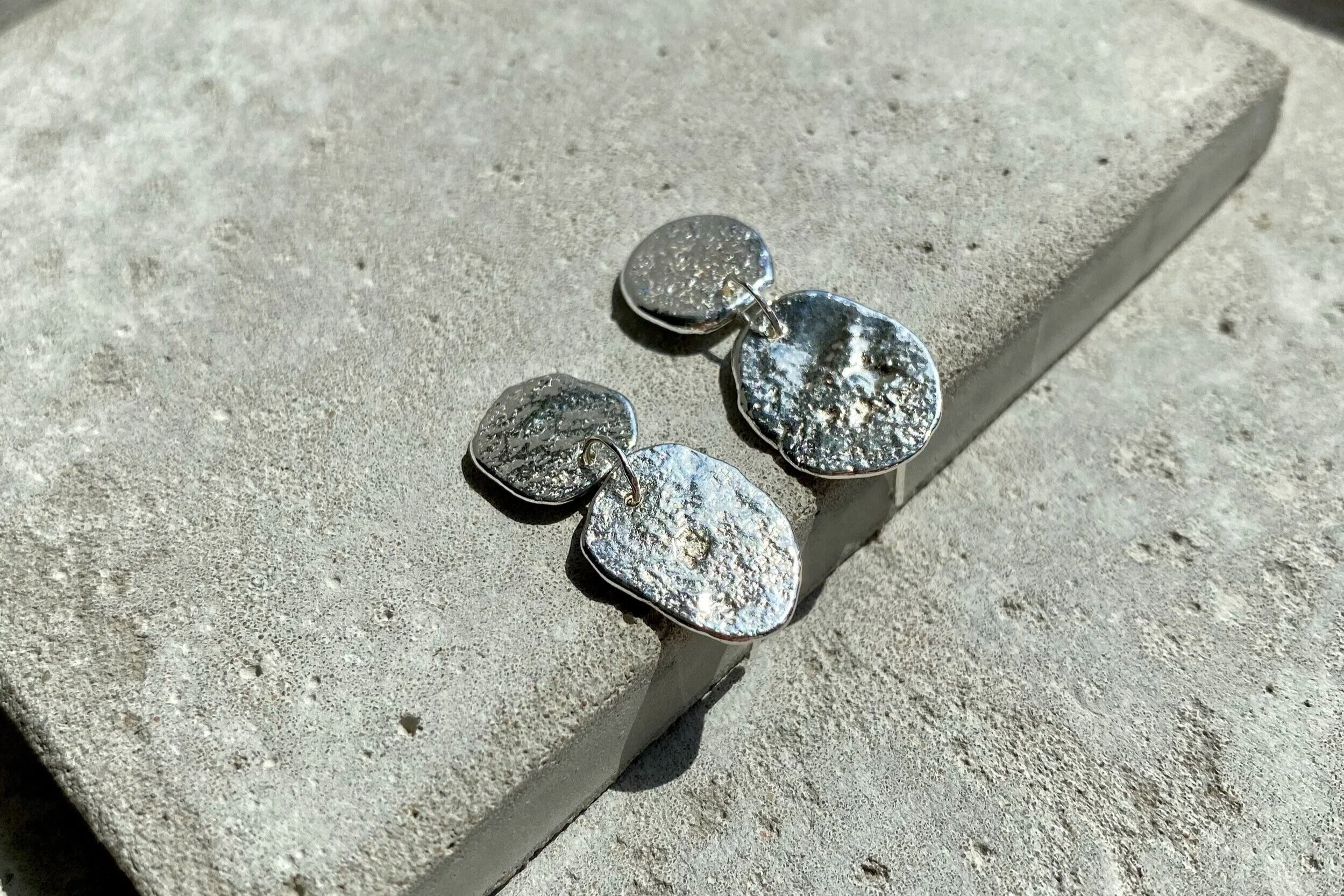 Silver earrings with hammered textured design, resting on a concrete surface.