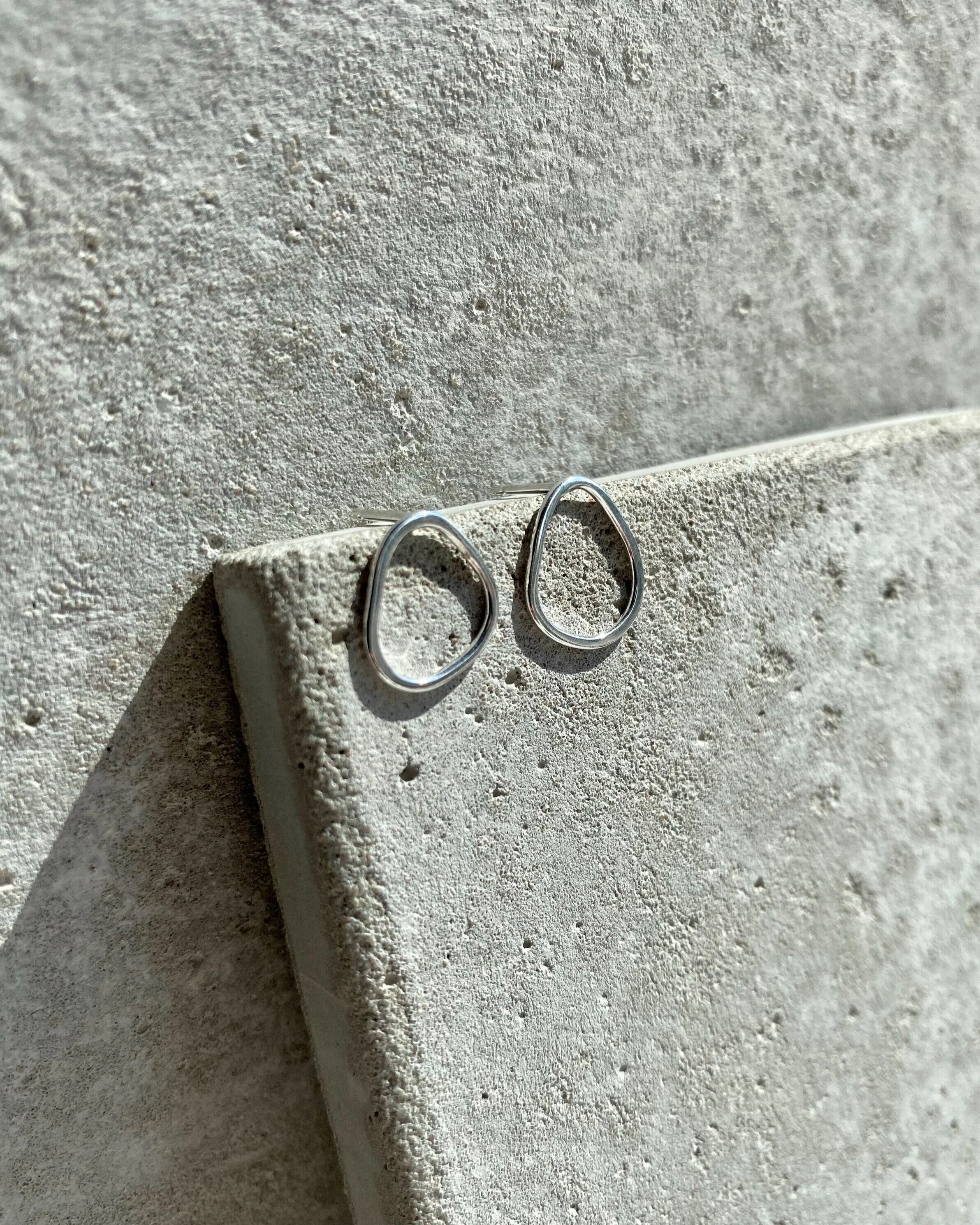 Close-up of two minimalist silver rings placed on a textured, light gray concrete surface.