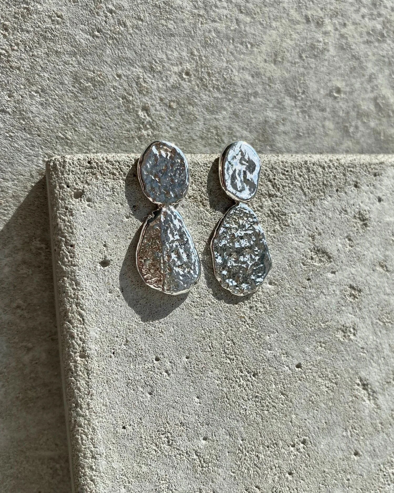 Pair of silver textured drop earrings on a beige textured surface.