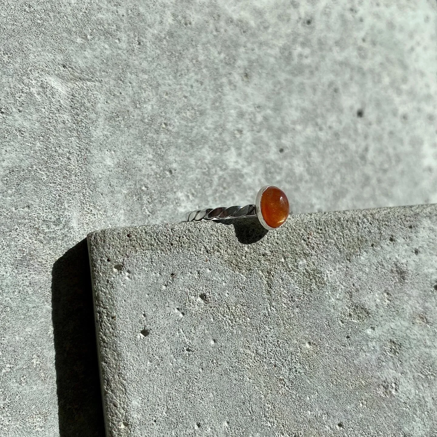 A silver twisted band ring with a round amber gemstone on a concrete surface.