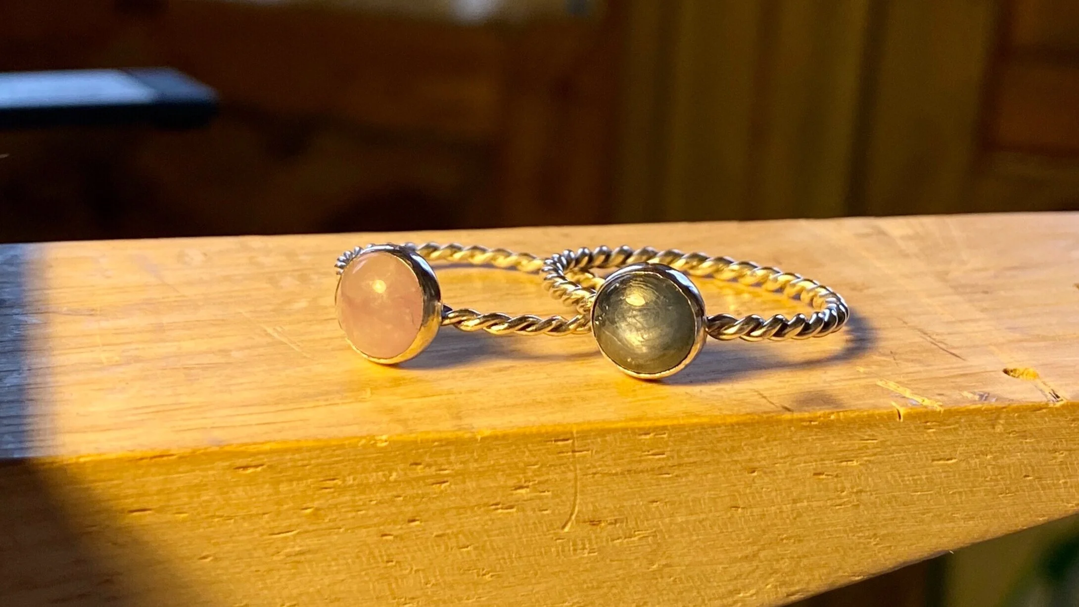 Silver twist bracelet with two circular stone settings, one with a pink stone and the other with a darker stone, on a wooden surface.