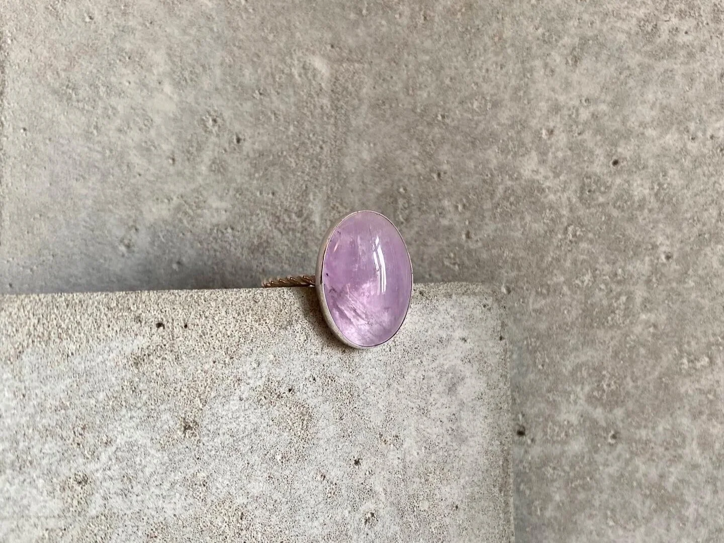 Ring with a large pink oval gemstone on a textured stone surface.