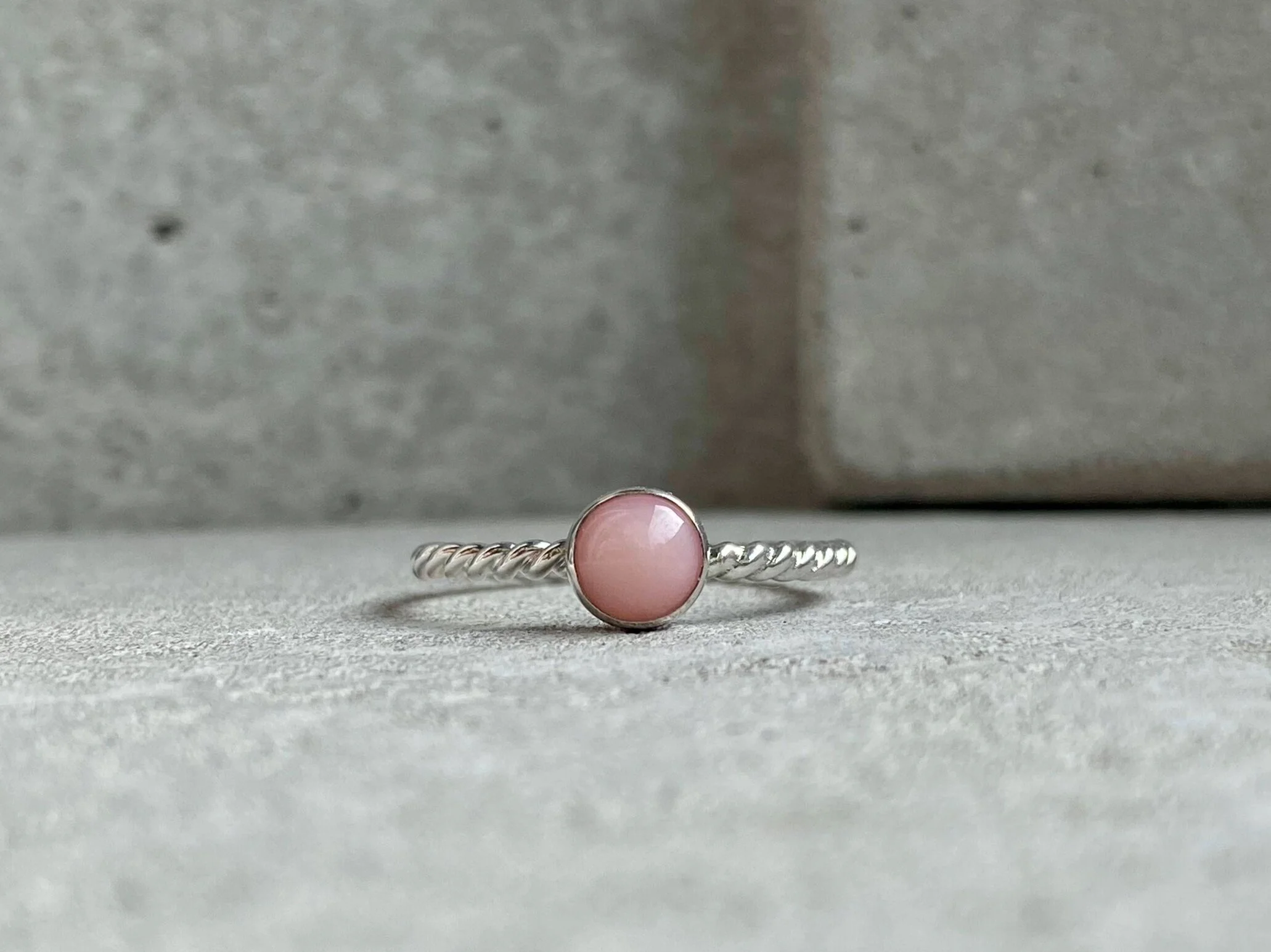 Silver ring with a pink round stone on a concrete surface with gray background.