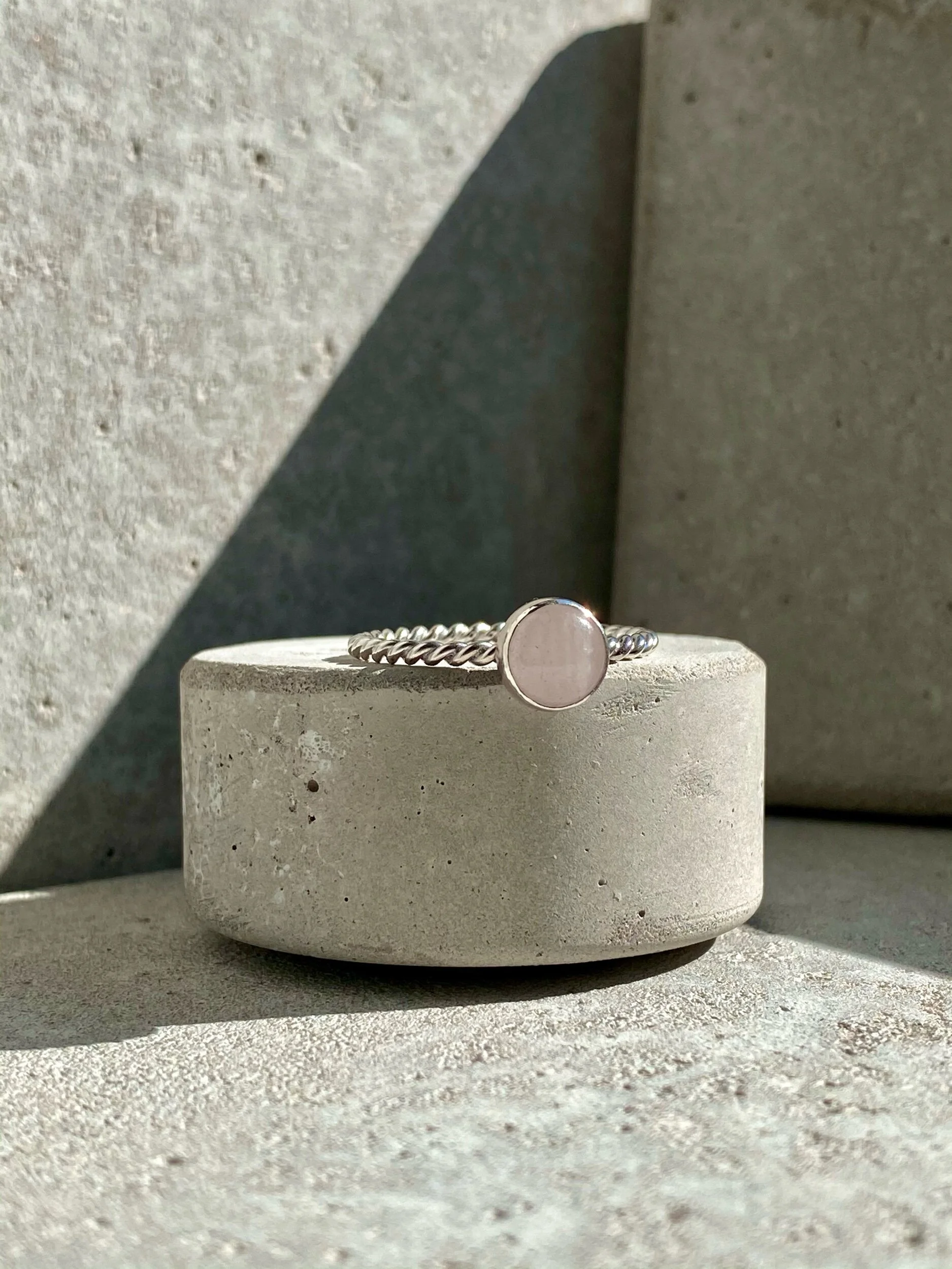 Silver bracelet with a round pale pink stone on a concrete block, sunlight casting shadows.
