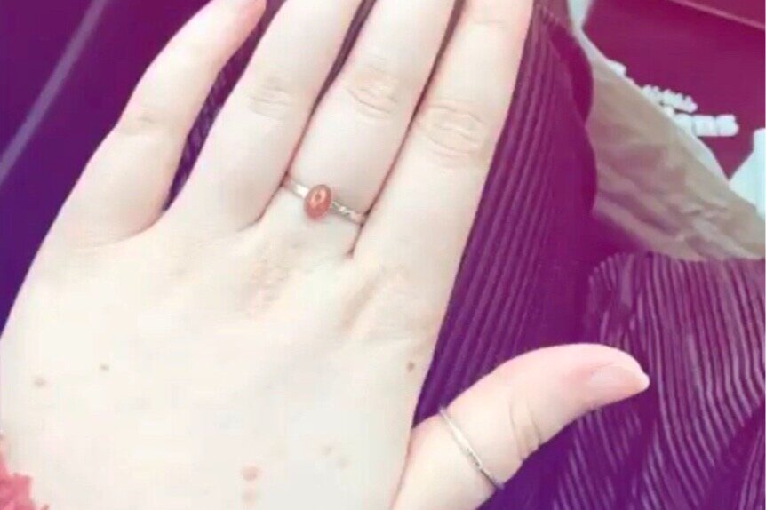 Close-up of a hand with a ring featuring a red oval-shaped gemstone, resting on a maroon velvet fabric.