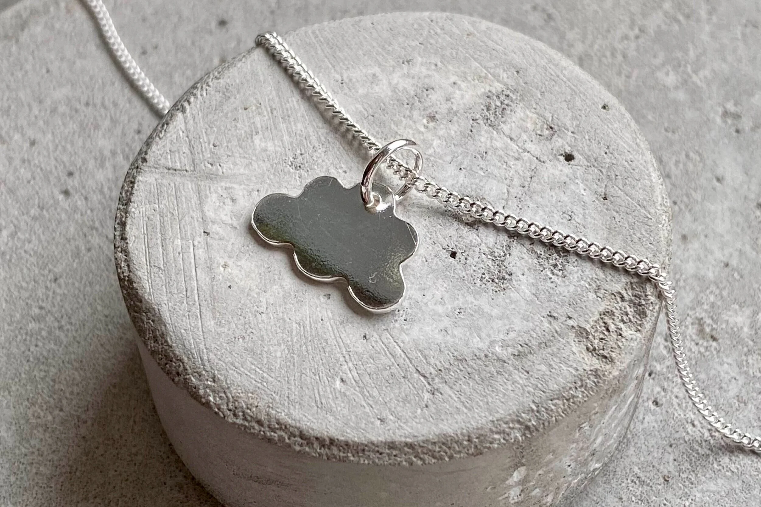 Silver necklace with a cloud-shaped pendant on a round concrete surface.