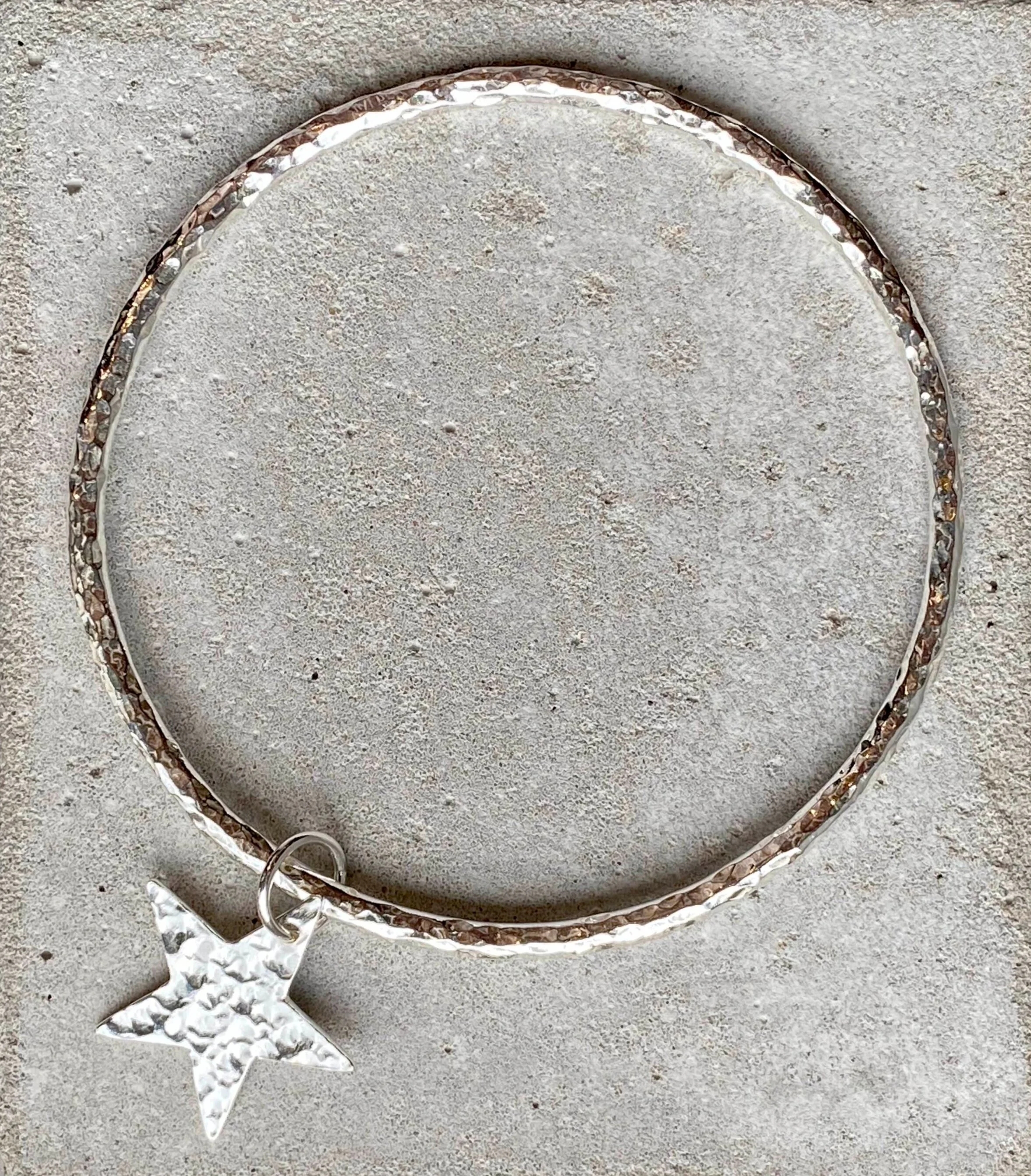 Silver bracelet with a star charm on a textured surface.